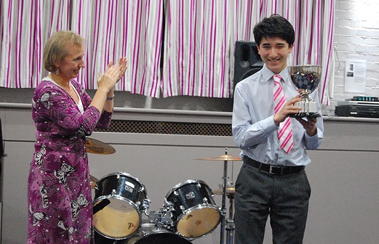 Boy holding trophy being applauded by judge