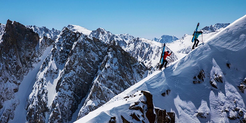 Two people climbing up a snowy mountain range