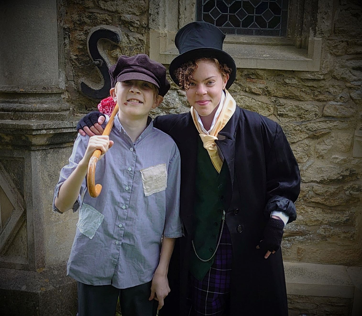 The Artful Dodger with his arm round Oliver's shoulders in front of a stone wall.