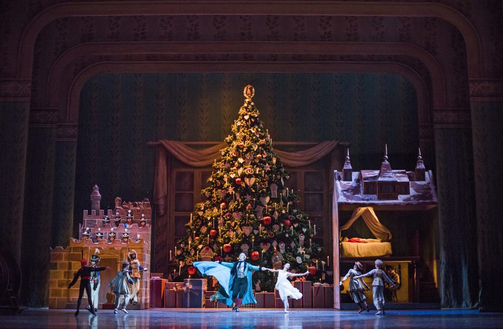 Clara and the Nutcracker dancing on stage in front of a big Christmas tree.