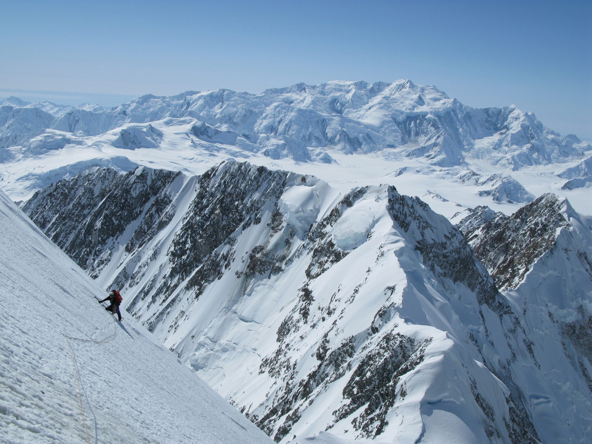 A landscape picture of snowy mountains with someone in the distance climbing them.