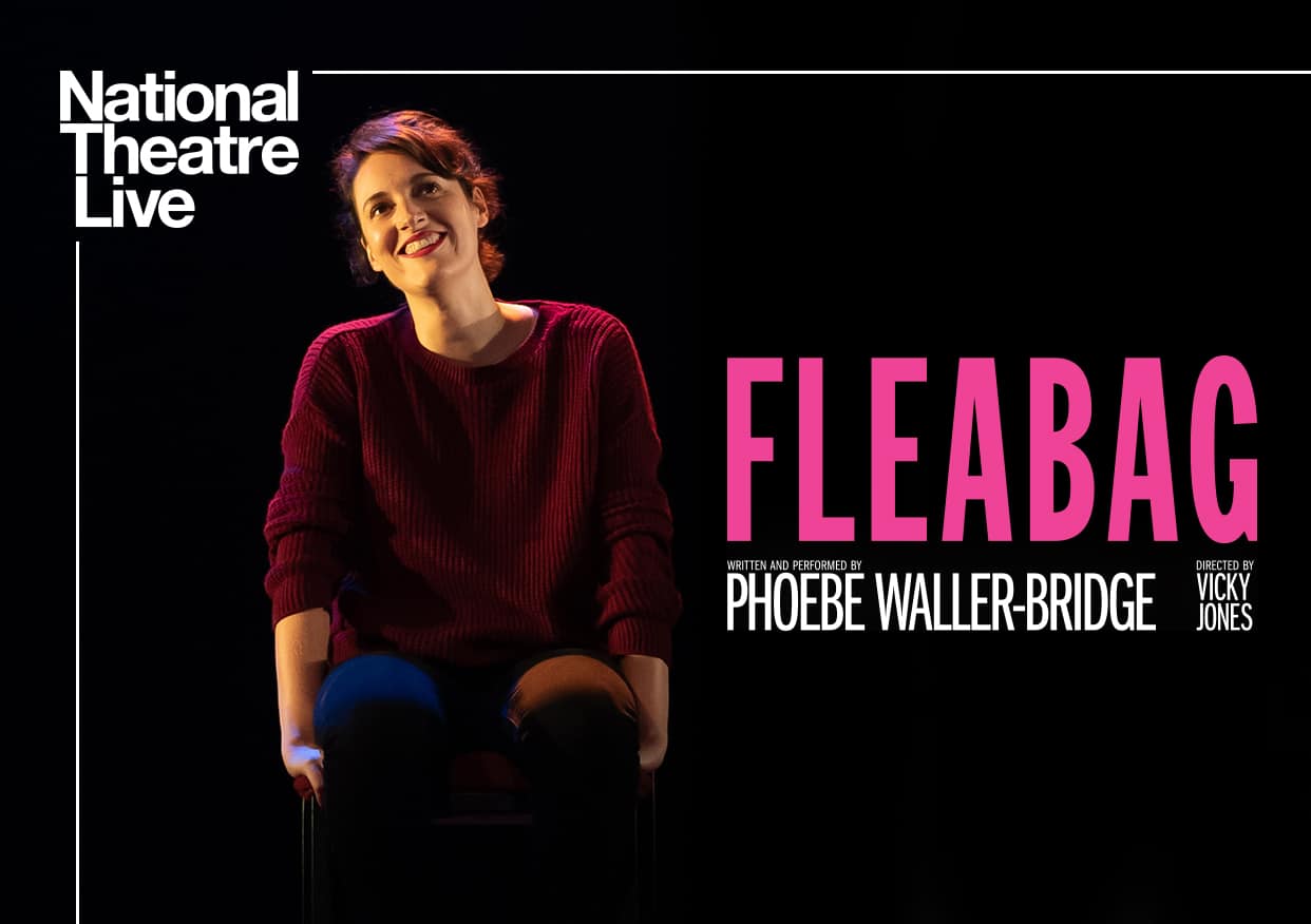 Phoebe Waller-Bridge smiling and sitting on her hands against a black background.