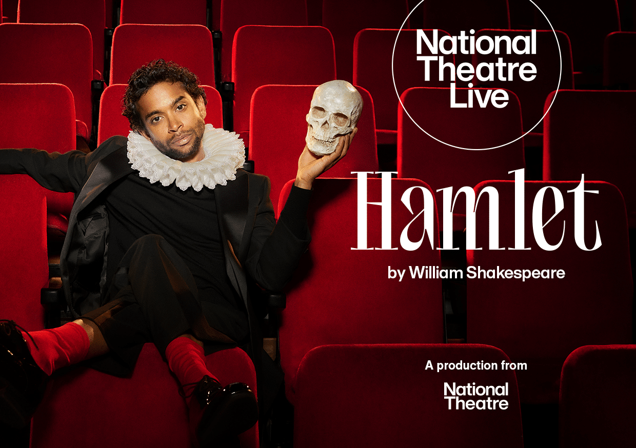 Actor playing Hamlet sat in an auditorium of red chairs holding a skull